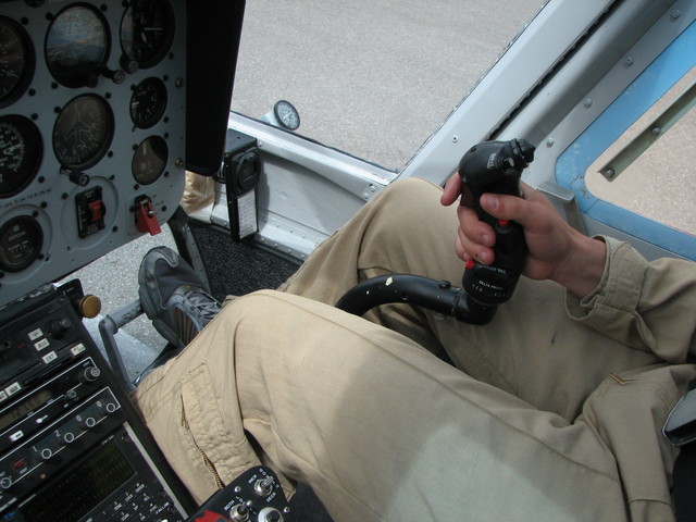 The controls. Anti-torque (tail rotor control) pedals, and cyclic control stick (for direction). The collective lever (for up/down) is in his left hand.